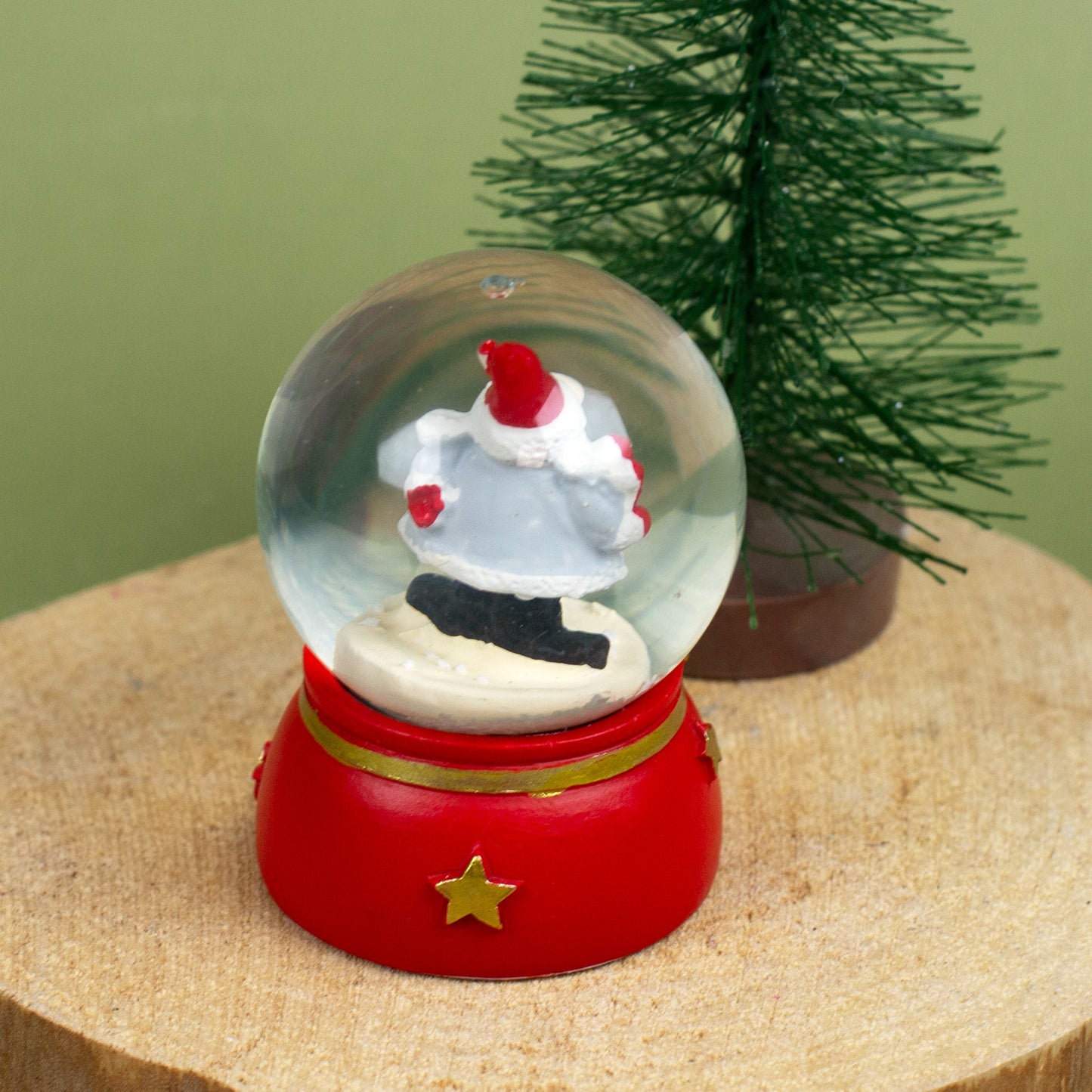 Schneekugel mit Weihnachtswichtel, der ein rotes Herz in den Händen hält, auf Holzuntergrund dekoriert