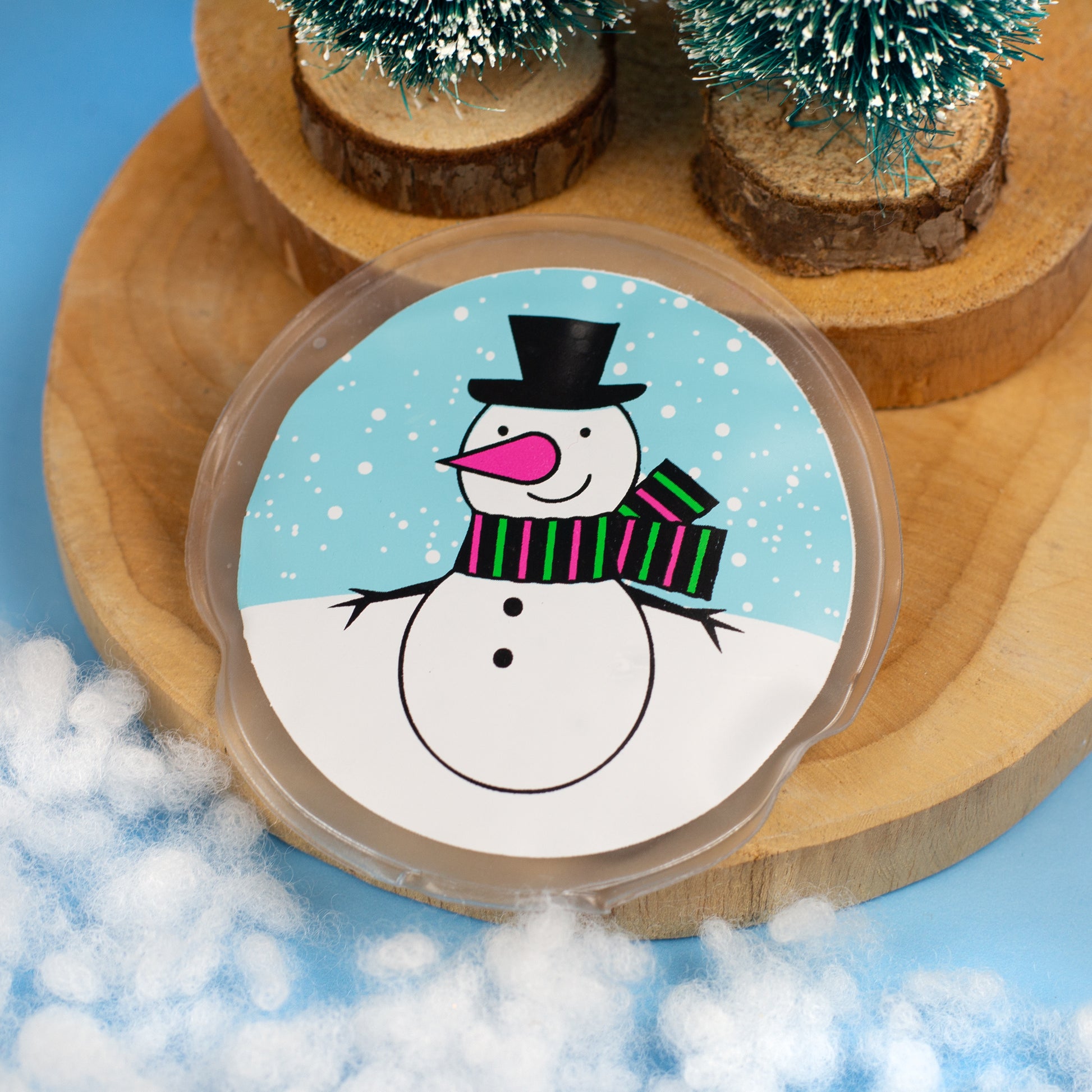 Runder Handwärmer mit Schneemannmotiv auf Holzunterlage und Kunstschnee