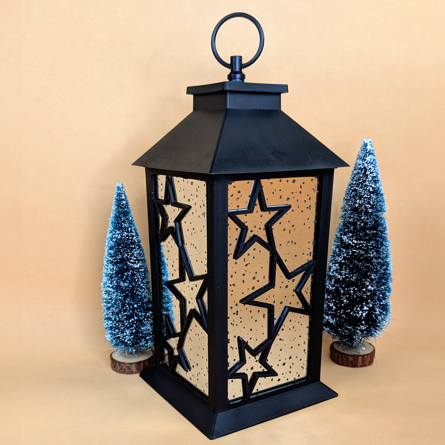 Schwarze LED-Laterne mit Sternenmuster als Weihnachtsdeko aufgestellt zwischen Tannenbäumchen