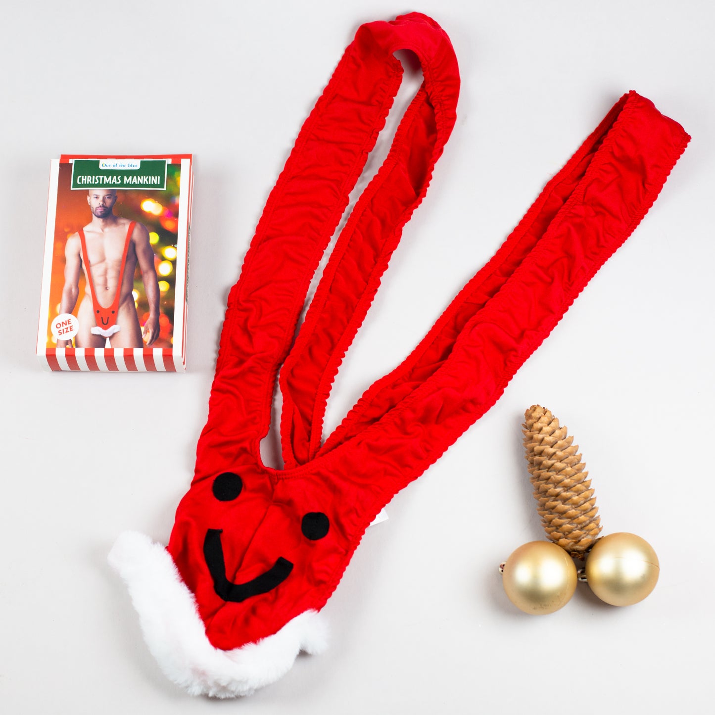 Roter Weihnachts-Mankini flach auf hellem Hintergrund, Verpackung daneben.