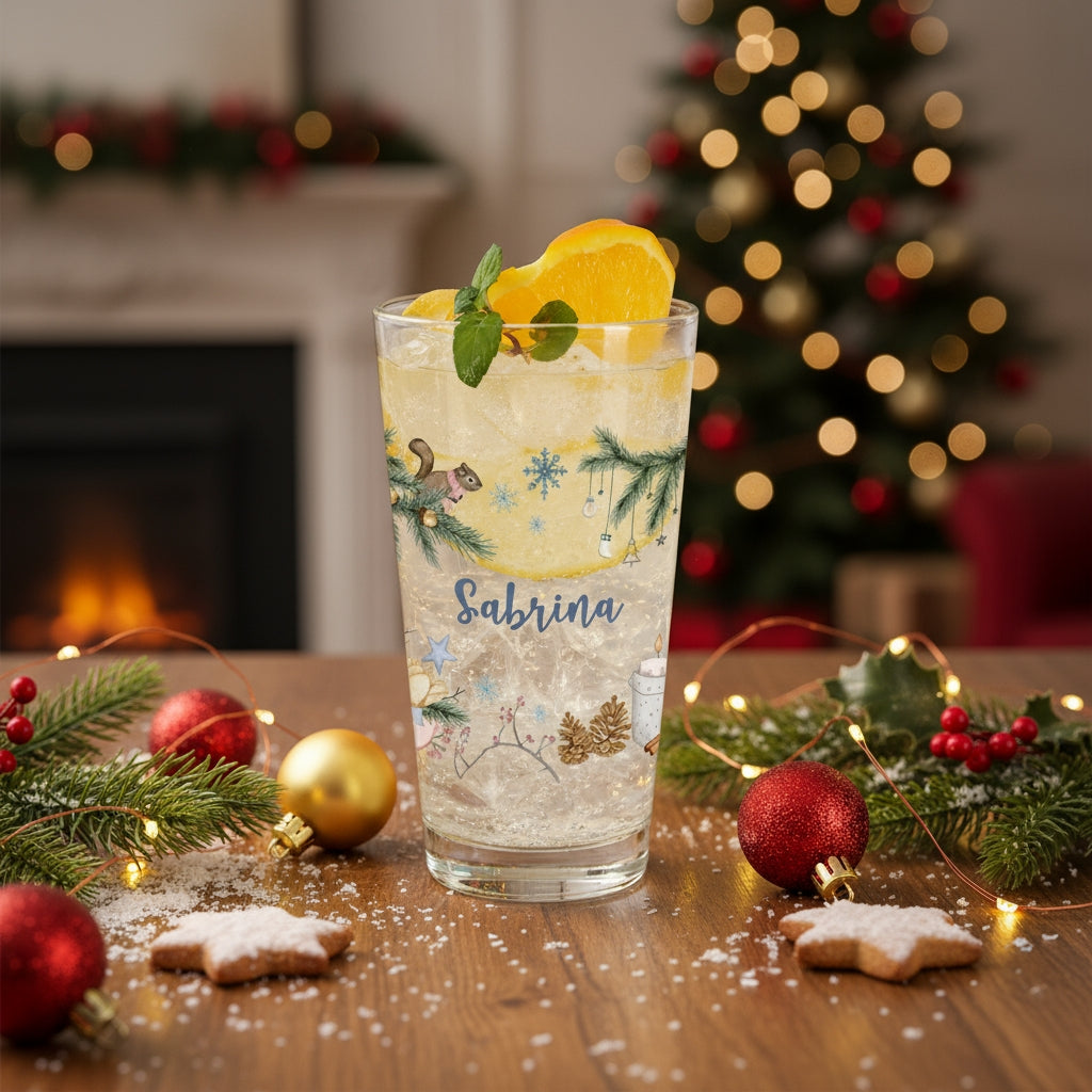 Festlich dekoriertes Trinkglas mit Weihnachtsmotiv und Name „Sabrina“ auf weihnachtlich geschmücktem Tisch vor einem Kamin