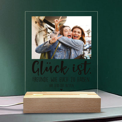 LED-Lampe mit dem Schriftzug „Glück ist,“ einem personalisierten Foto und zwei Zeilen Wunschtext vor grüner Wand.