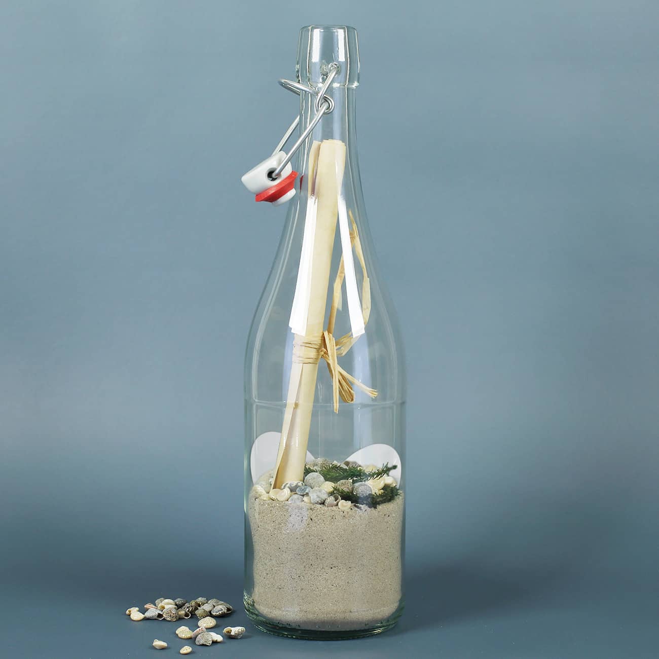Gefüllte Flaschenpost mit Sand, Muscheln, Grün und Papier