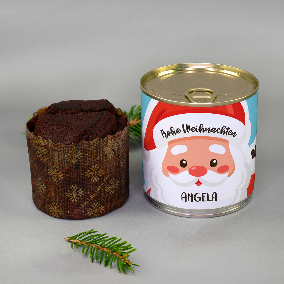 Personalisierter Weihnachts-Dosenkuchen mit Wunschname und ausgepacktem Brownie neben Tannenzweig als festliches Geschenk