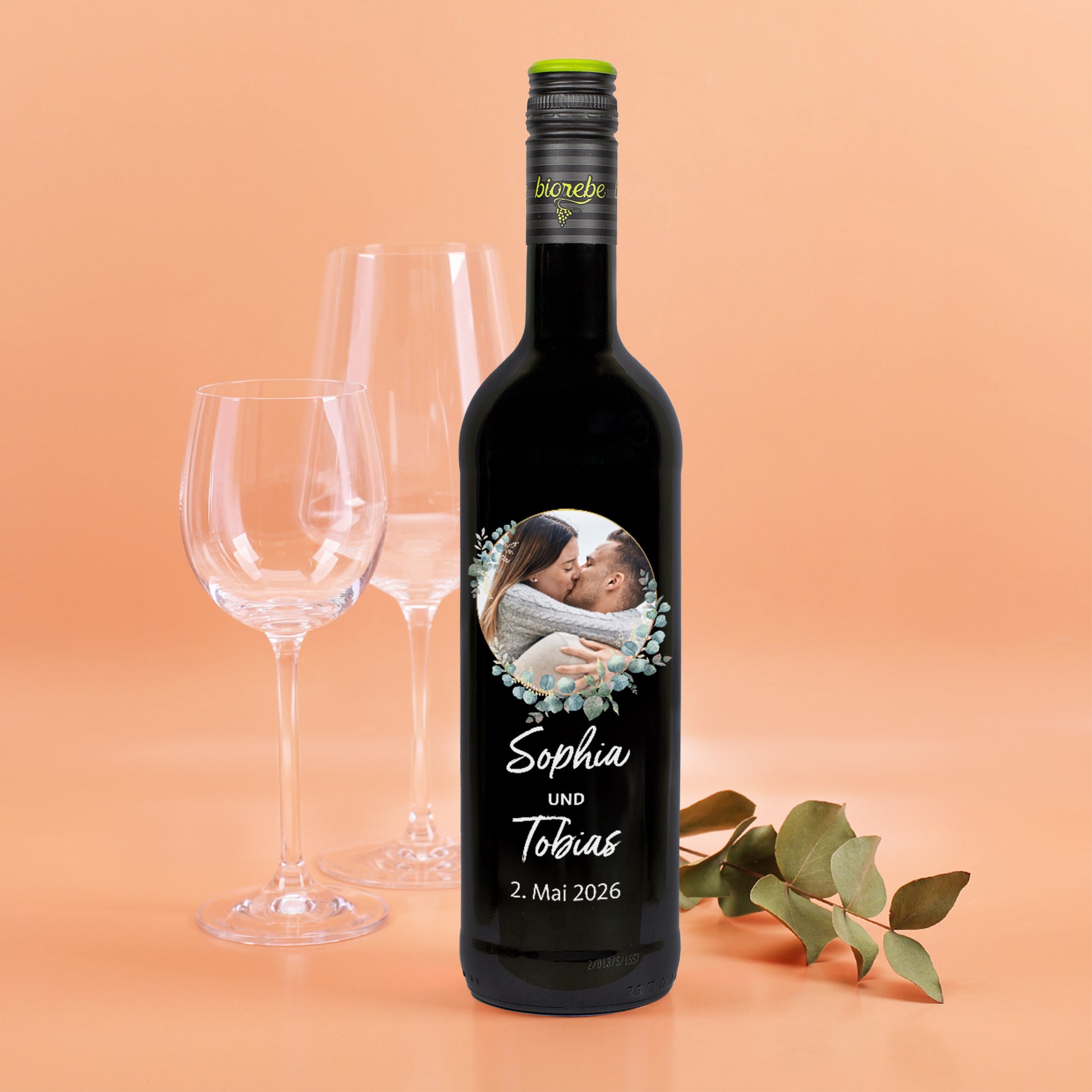 Personalisierte Rotweinflasche mit Foto und Eukalyptuskranz, Namen „Sophia und Tobias“ und Hochzeitsdatum.