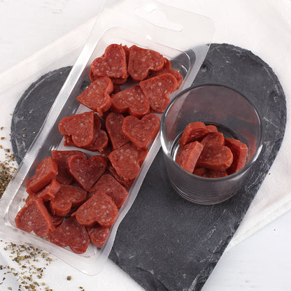 Geöffnete Verpackung mit Salami Herzen und Glas als herzhafter Snack für Männer