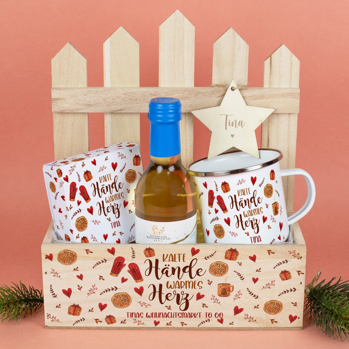 Komplettes Weihnachtsmarkt-to-Go Set in einem bedruckten Holzkasten mit winterlichem Motiv. Enthalten sind eine Mini-Flasche Winzerglühwein, eine personalisierte Metalltasse, eine Lindor-Geschenkverpackung mit identischem Motiv sowie ein gravierter Holzstern mit dem Namen „Selina“, befestigt an der Zaun-Deko im Hintergrund.