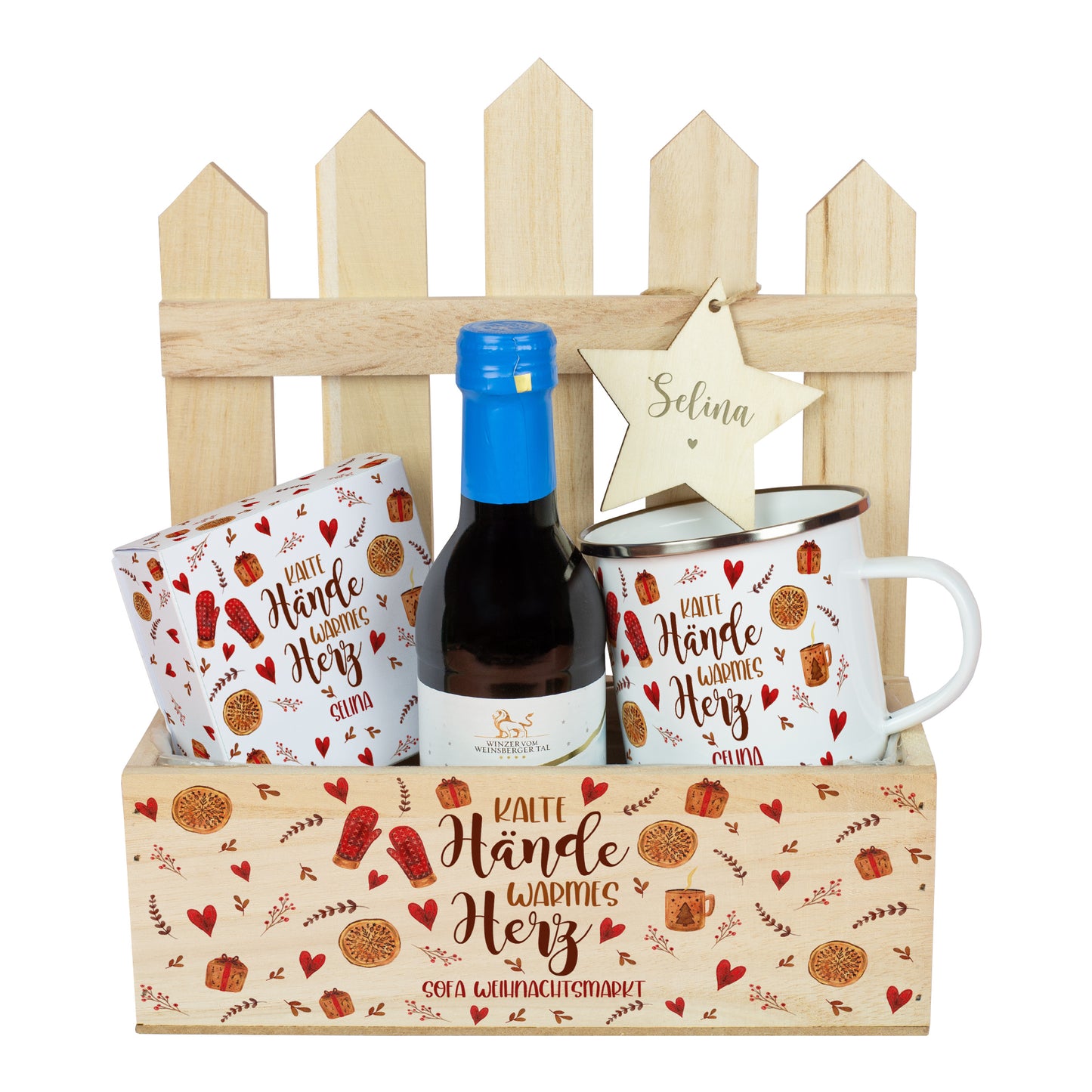 Geschenkkorb „Weihnachtsmarkt to Go“ mit Mini-Glühwein in Rot, Metalltasse, Lindor-Verpackung und personalisiertem Holzstern. Der Holzkasten zeigt den Spruch „Kalte Hände warmes Herz“ mit zusätzlichem Wunschtext auf der Vorderseite, arrangiert vor Zaun-Deko.