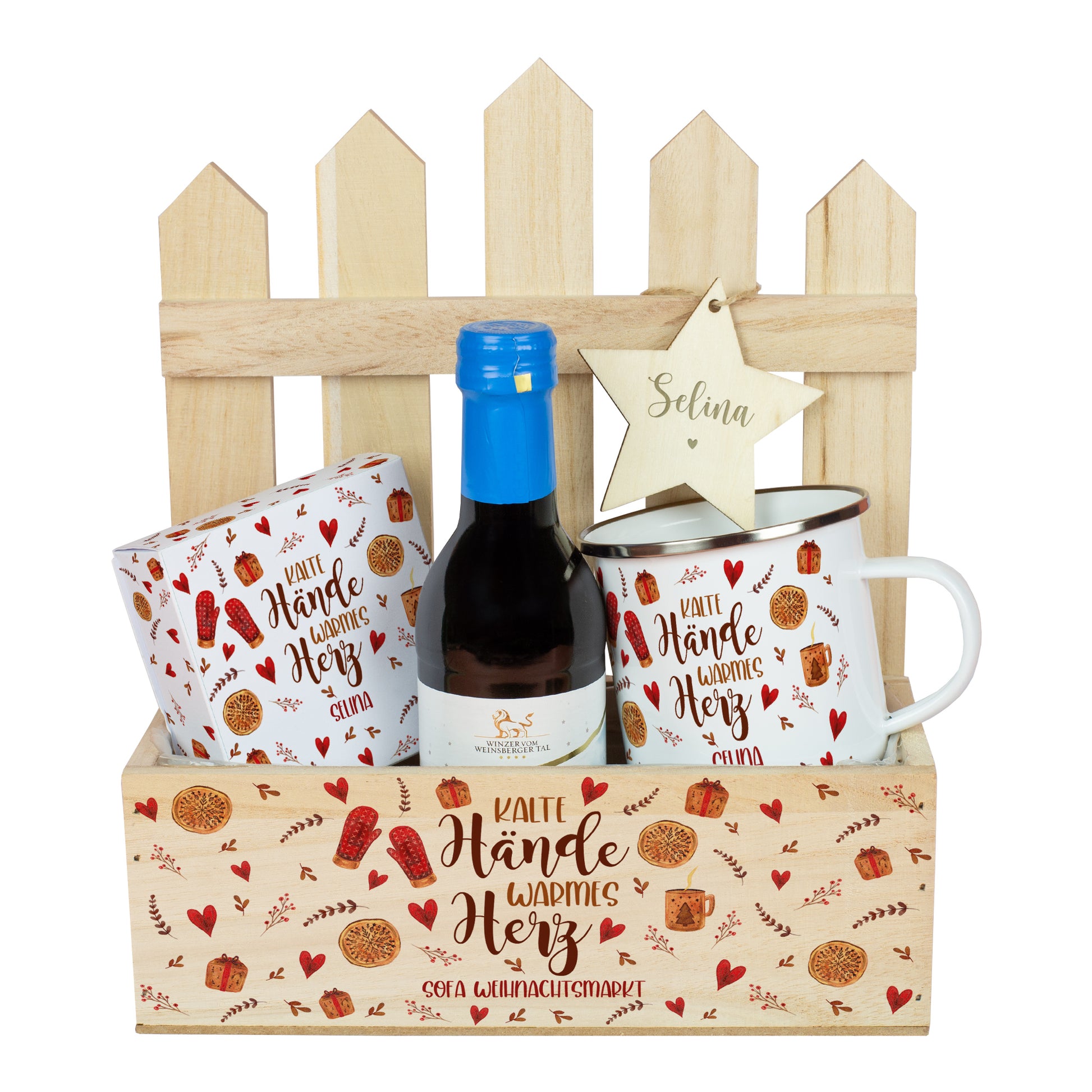Geschenkkorb „Weihnachtsmarkt to Go“ mit Mini-Glühwein in Rot, Metalltasse, Lindor-Verpackung und personalisiertem Holzstern. Der Holzkasten zeigt den Spruch „Kalte Hände warmes Herz“ mit zusätzlichem Wunschtext auf der Vorderseite, arrangiert vor Zaun-Deko.
