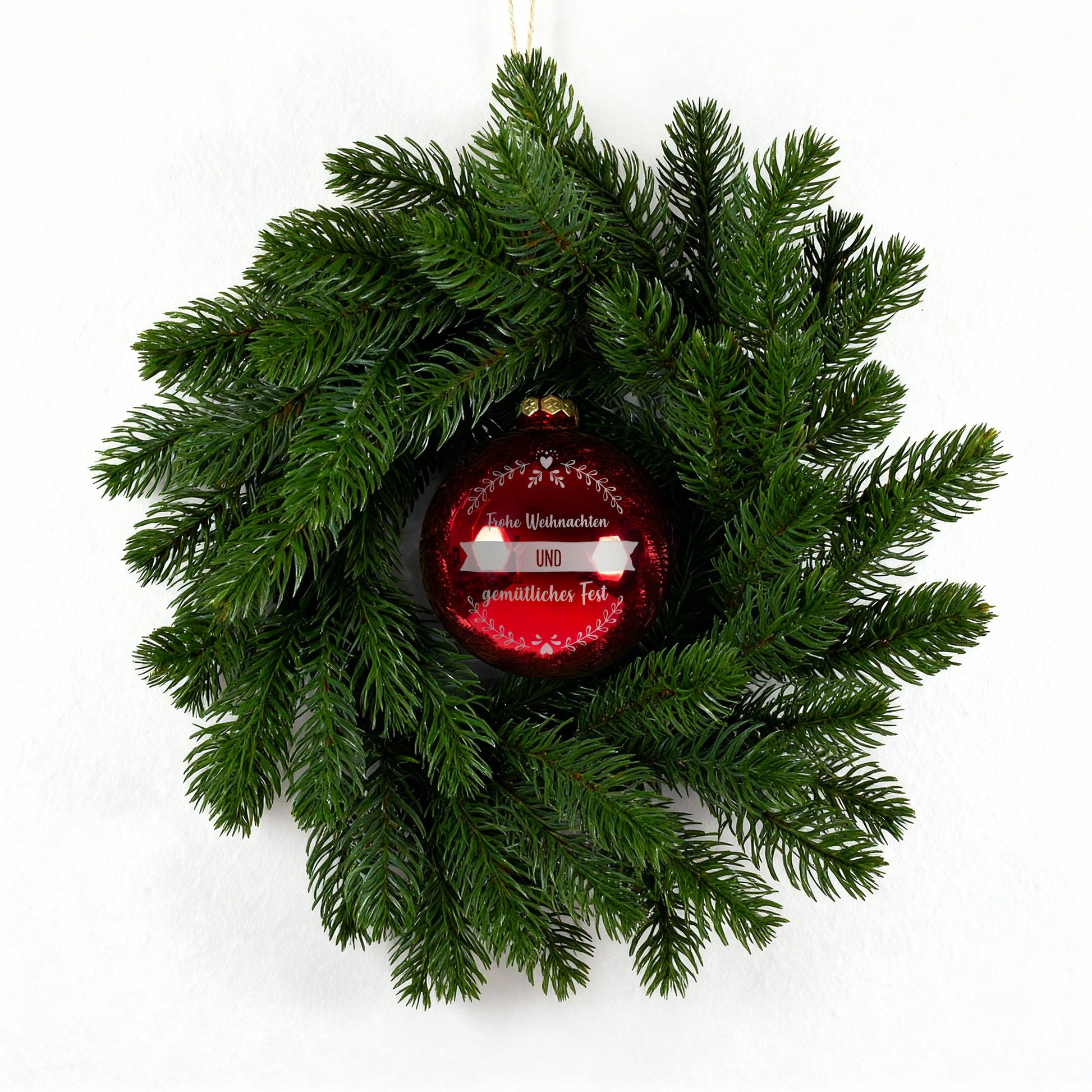 Kunst-Tannenkranz mit roter gravierter Weihnachtskugel vor hellem Hintergrund
