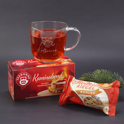 Geschenkset mit personalisierter Glastasse, Tee und Stollen vor dunklem Hintergrund und Tannenzweig