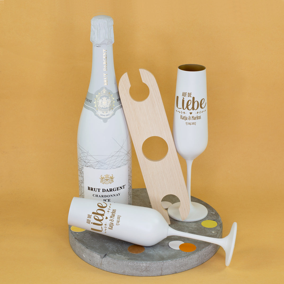 Brut Dargent Chardonnay mit personalisierten Sektgläsern für Katja & Markus, Gravur Auf die Liebe und Hochzeitsdatum 17.04.2027 neben Weinbutler aus Akazienholz
