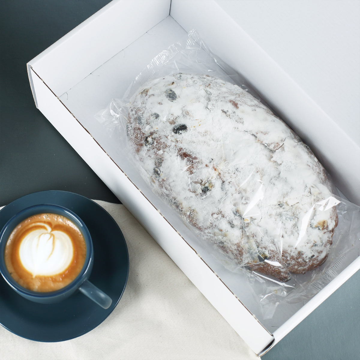 1000 g Rosinenstollen in geöffneter Geschenkbox neben einer Tasse Kaffee