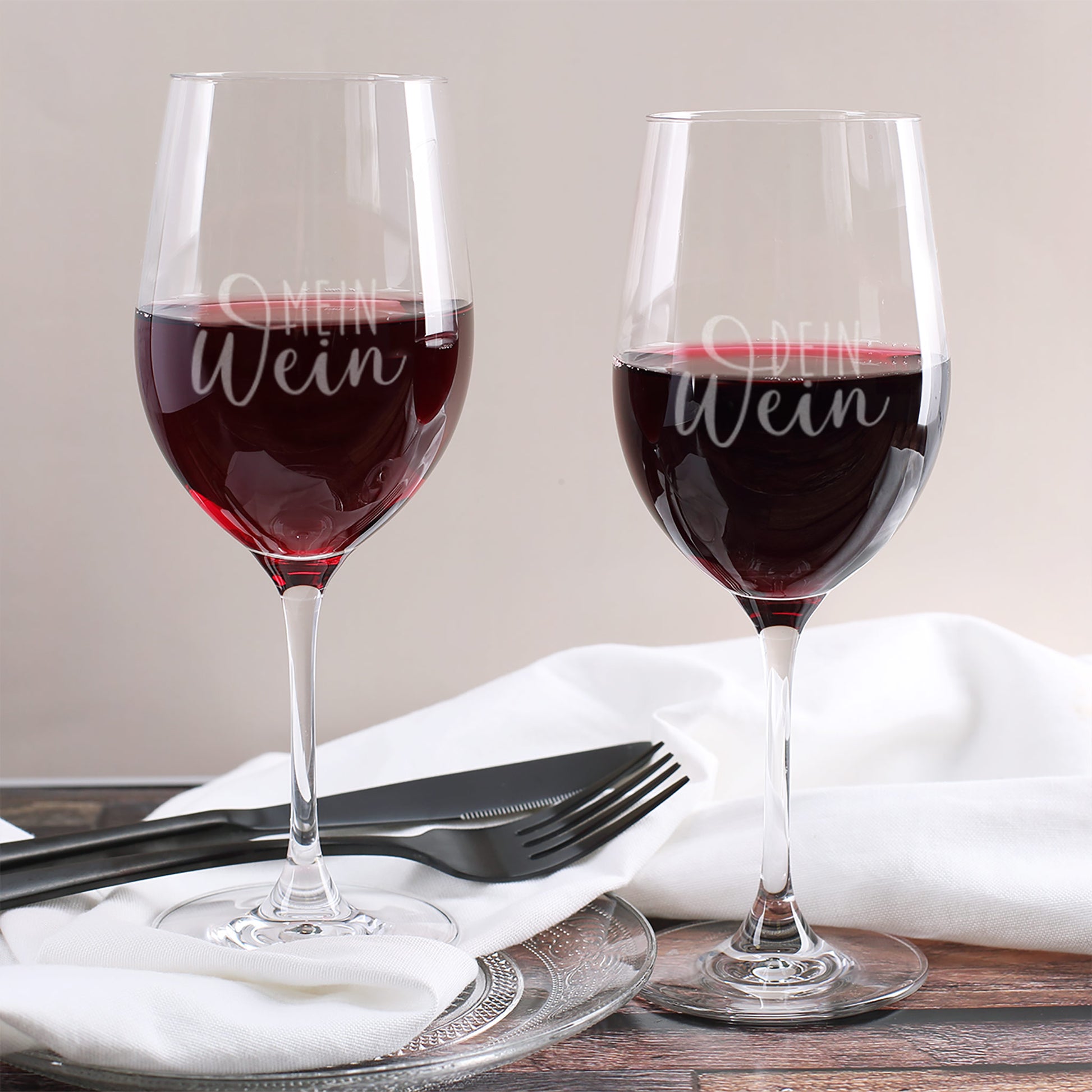 Zwei gravierte Weingläser mit den Aufschriften „Mein Wein“ und „Dein Wein“, gefüllt mit Rotwein