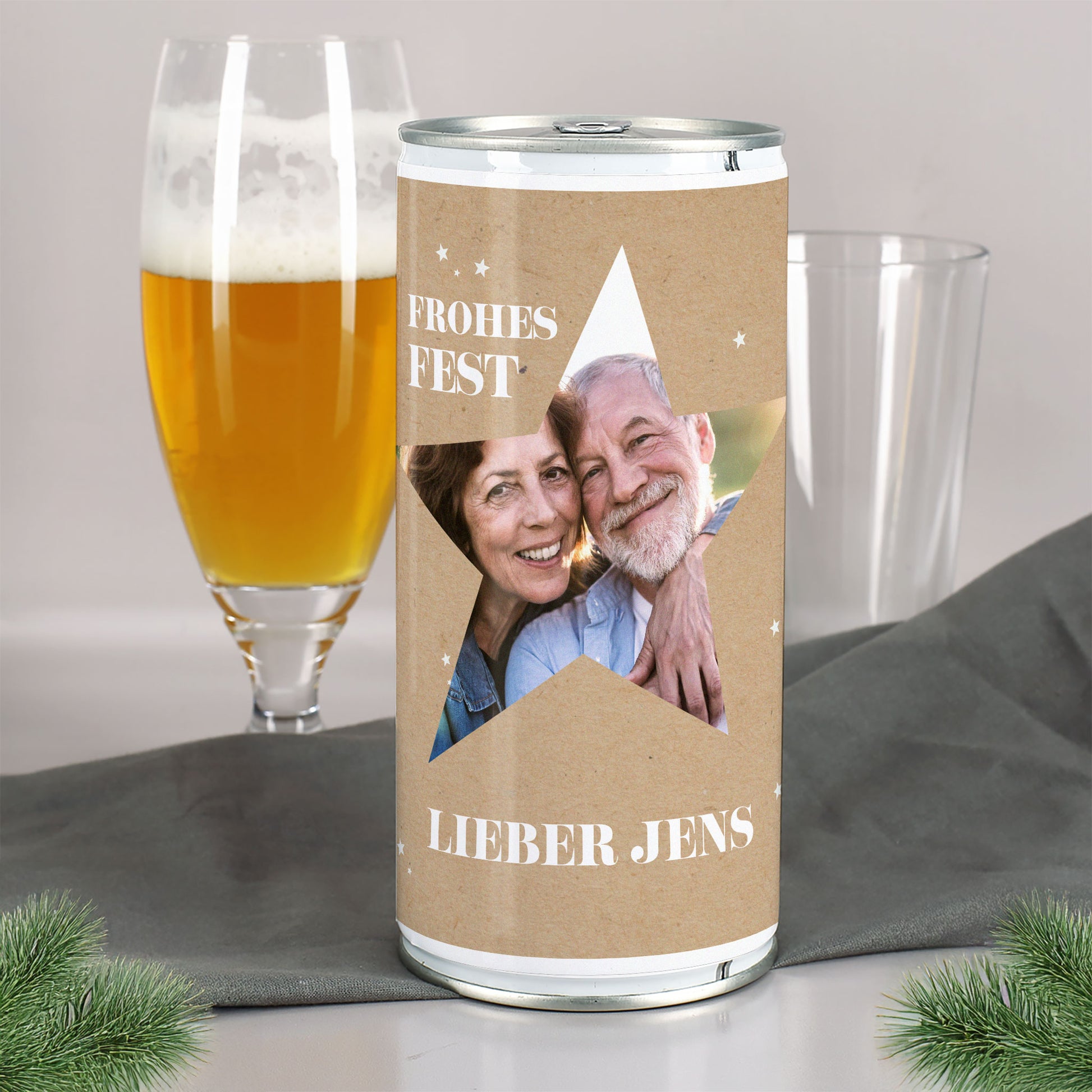 Große personalisierte Bierdose mit Stern-Ausschnitt und Paarfoto, Aufdruck „Frohes Fest“ und Name „Lieber Jens“, neben Bierglas und Tannenzweigen.