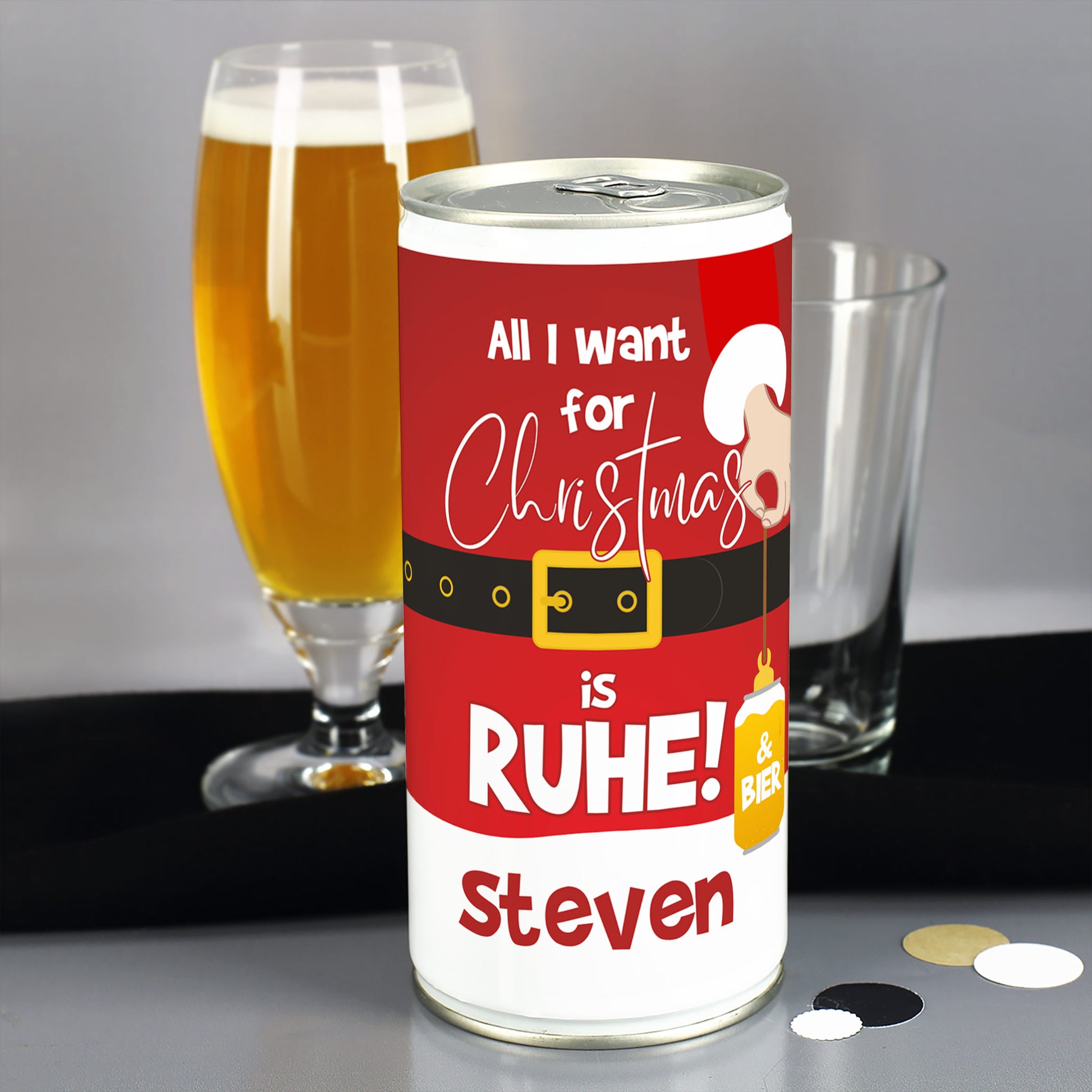 Weihnachtsbier-Dose mit personalisiertem Namen im Weihnachtsmann-Look, daneben gefülltes Bierglas und leeres Glas im Hintergrund.