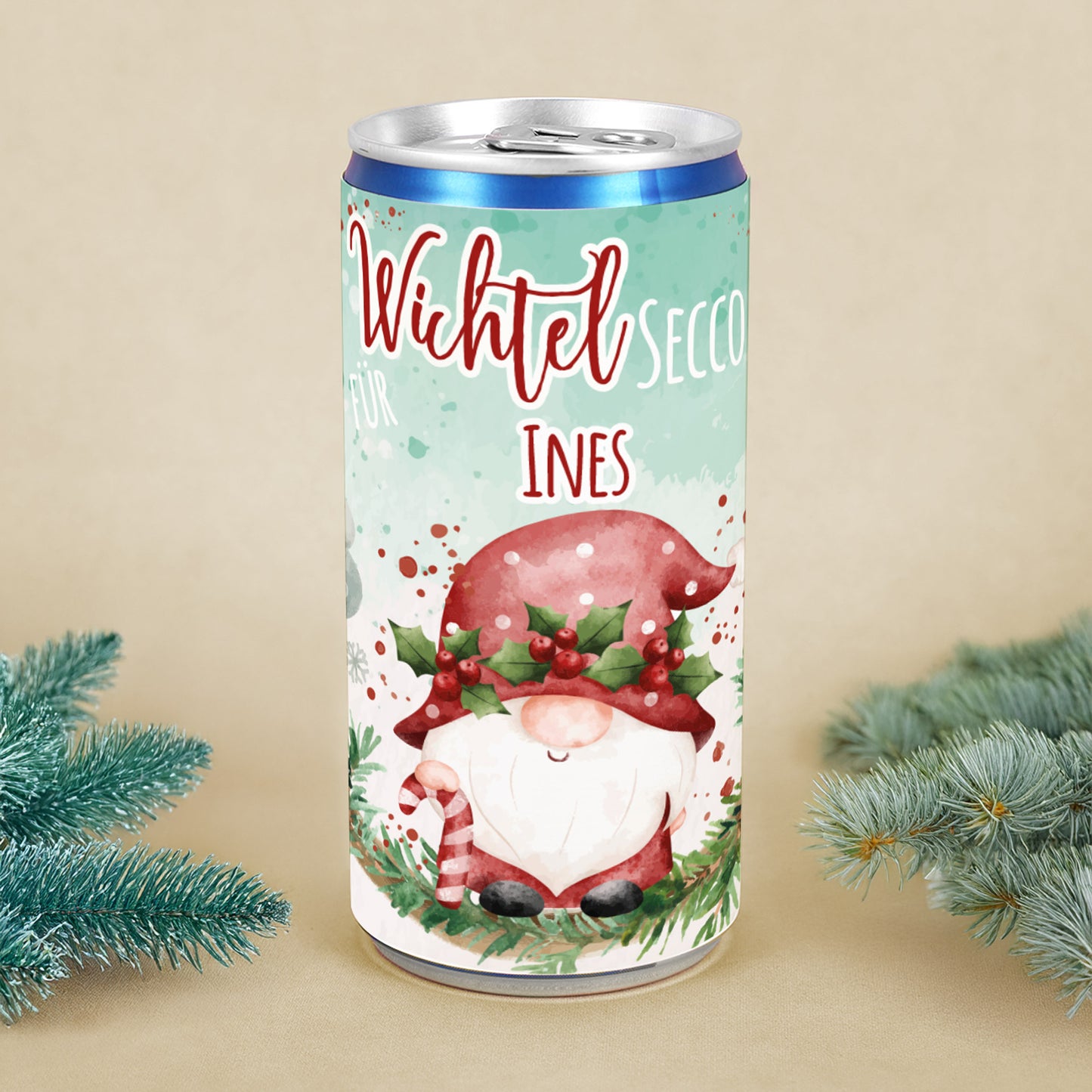 Personalisierte Secco-Dose mit Wichtelmotiv, roter Mütze, Mistelkranz und Name Ines, dekoriert mit Tannenzweigen als Weihnachtsgeschenk.