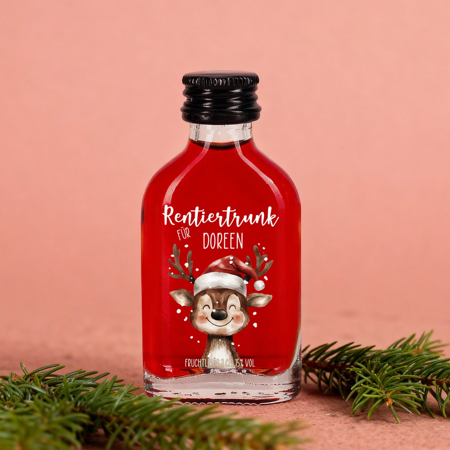 Fruchtlikör-Flasche „Rentiertrunk für Doreen“ auf rosafarbenem Hintergrund mit Tannengrün, winterliche Szene mit rotem Likör und liebevollem Etikett.