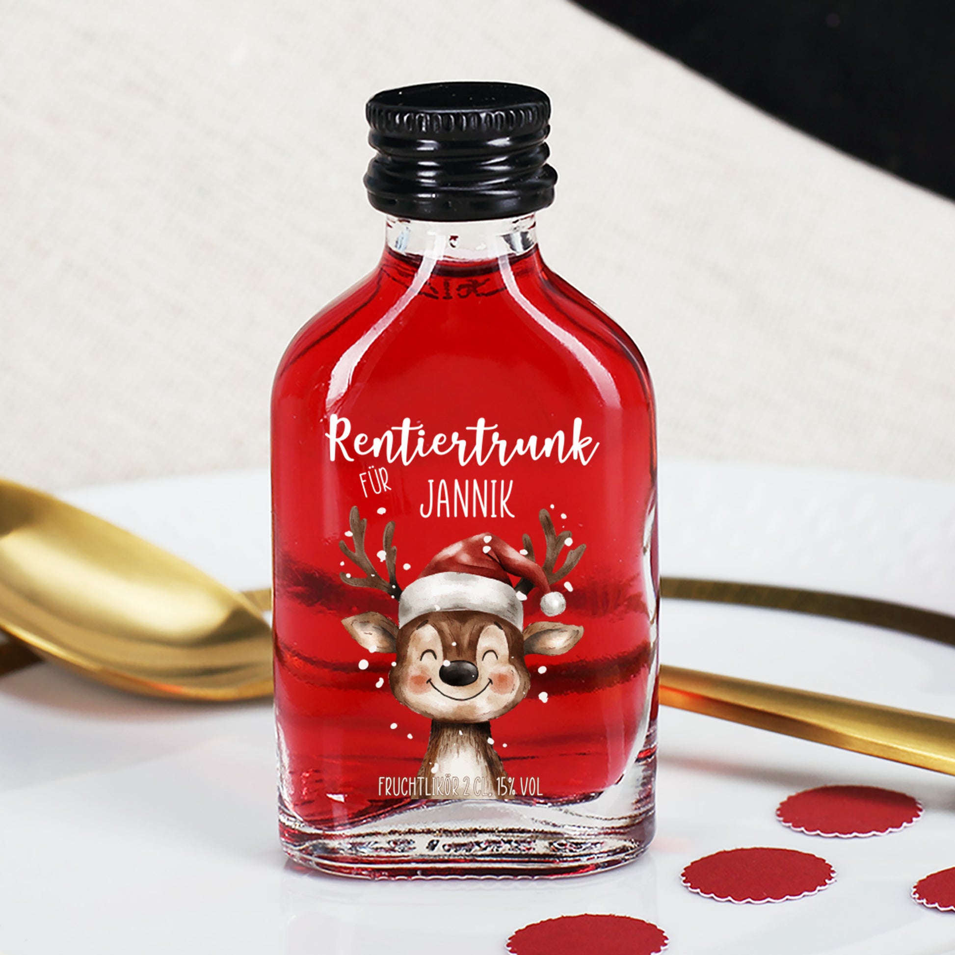 Roter Rentiertrunk mit Name Jannik, auf weißem Teller mit goldfarbenem Löffel und runden roten Deko-Elementen – festlich arrangiert.