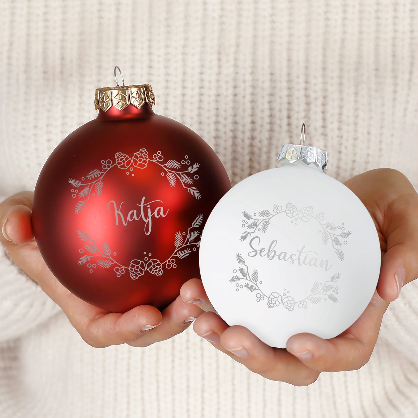 Zwei Weihnachtskugeln – Rot und Weiß – in matter und glänzender Ausführung mit Gravur „Katja“ und „Sebastian“, festlich dekoriert auf Tannenzweigen.