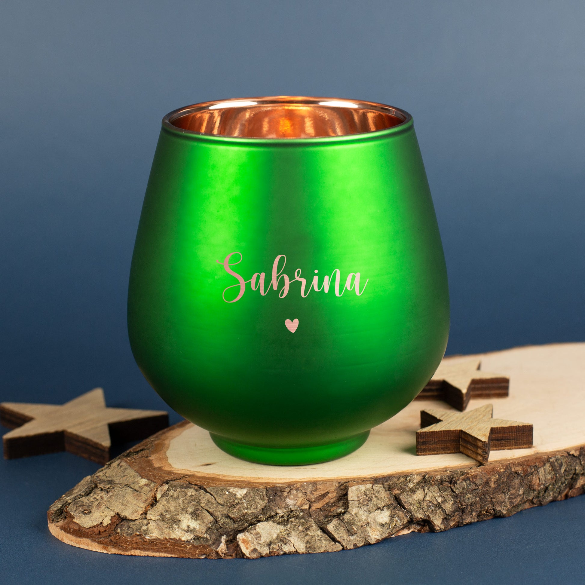 Grünes Windlicht mit Gravur „Sabrina“ und Herzsymbol, auf Holzscheibe mit kleinen Holzsternen arrangiert.