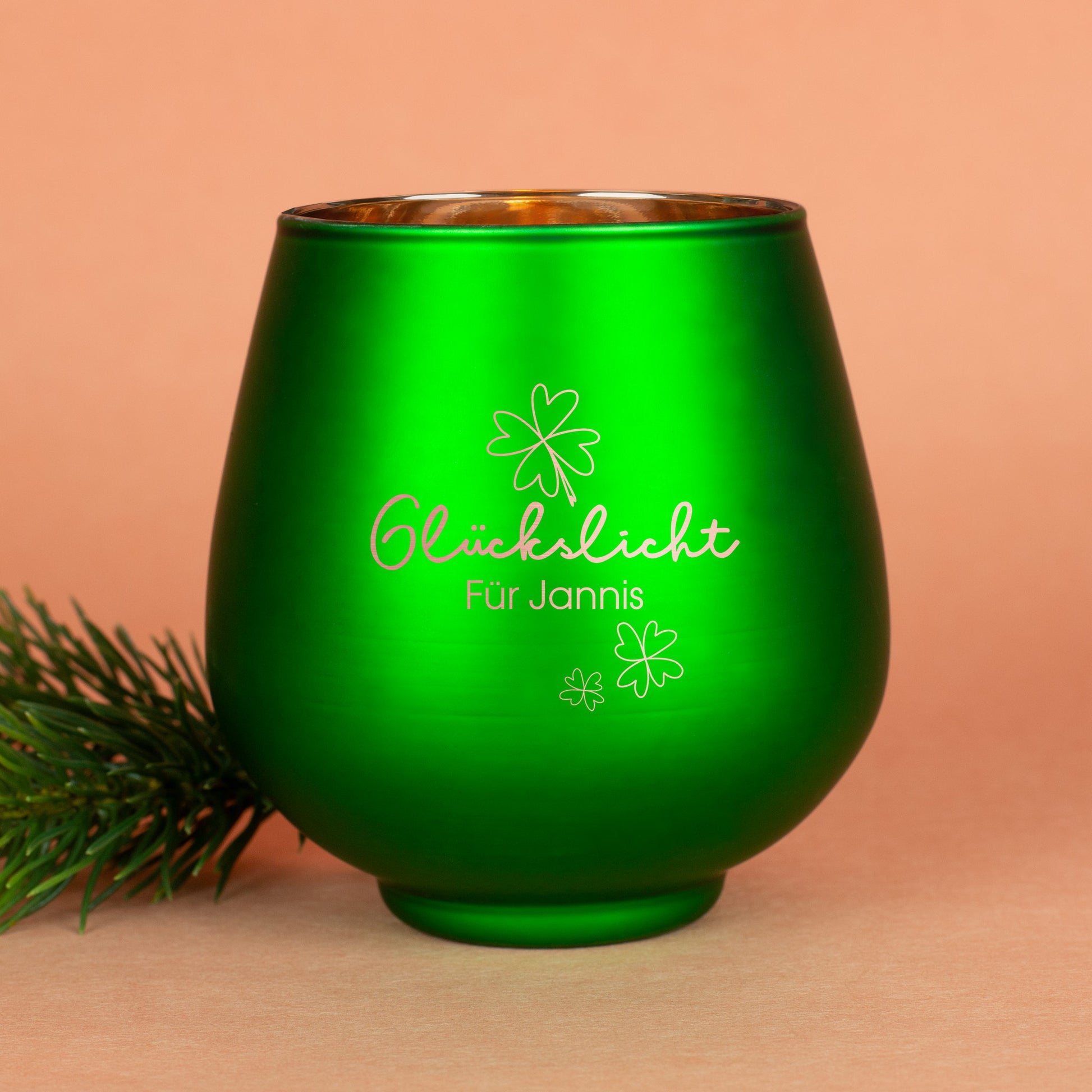 Grünes Windlicht mit Gravur „Glückslicht für Jannis“, auf hellem Hintergrund mit Tannenzweig
