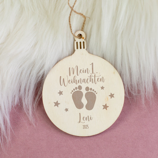 Holzanhänger „Mein 1. Weihnachten“ mit Namen und Jahr graviert, Motiv Babyfüße und Sterne, dekoriert auf weißem Fellhintergrund.