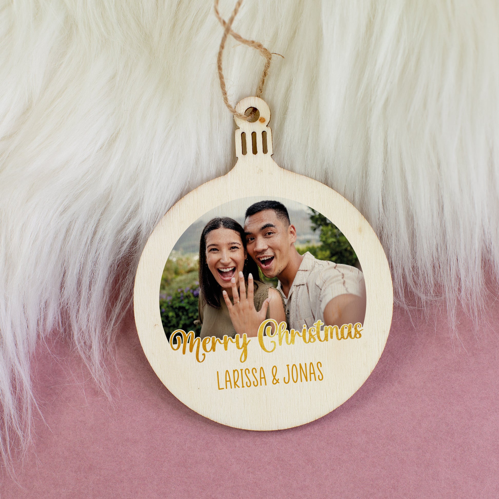 Personalisierter Christbaumschmuck mit Foto eines Paares und goldener Schrift „Merry Christmas Larissa & Jonas“ auf Felluntergrund.