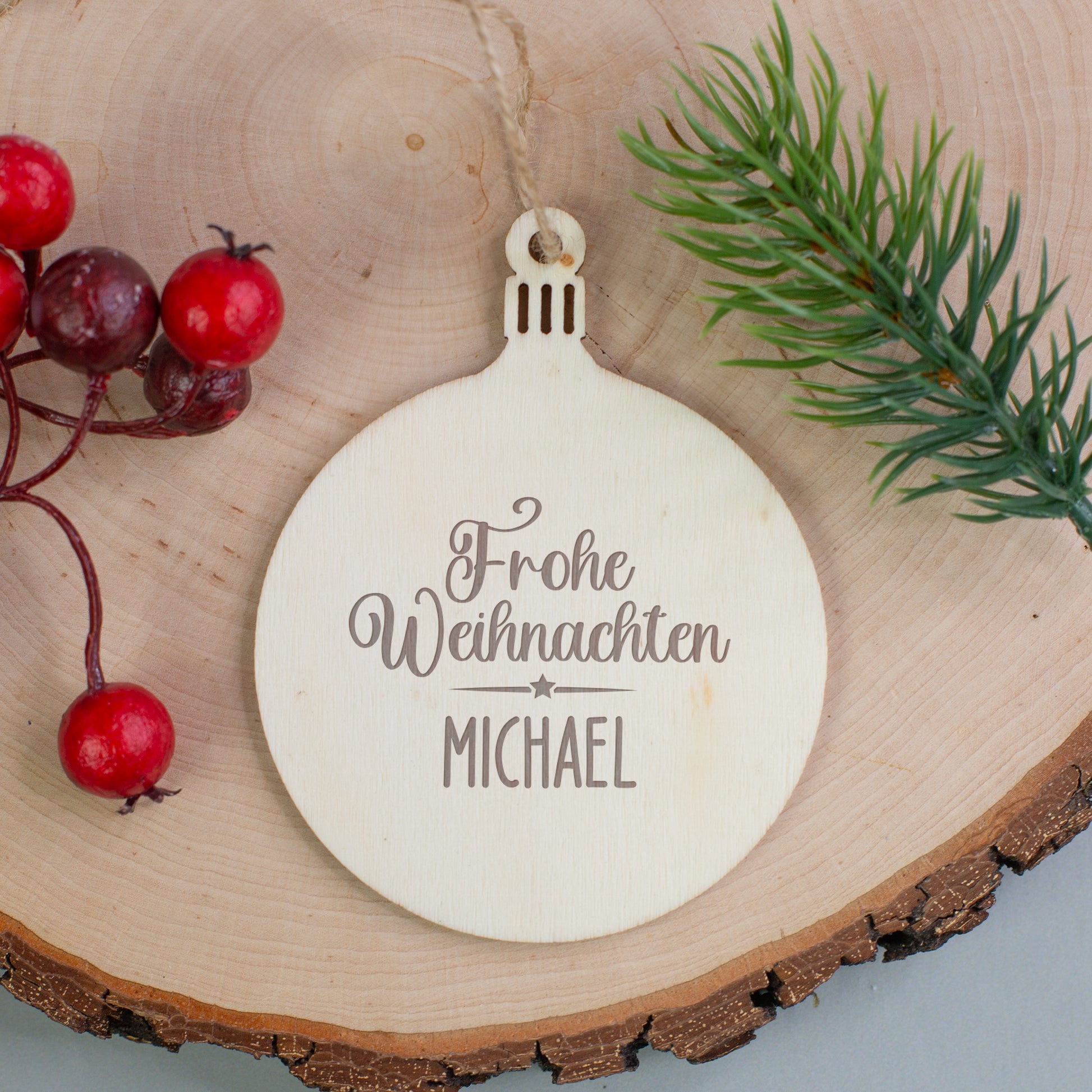 Holzanhänger Kugel mit Gravur „Frohe Weihnachten Michael“, auf Holzscheibe mit Beeren und Tannenzweig dekoriert.
