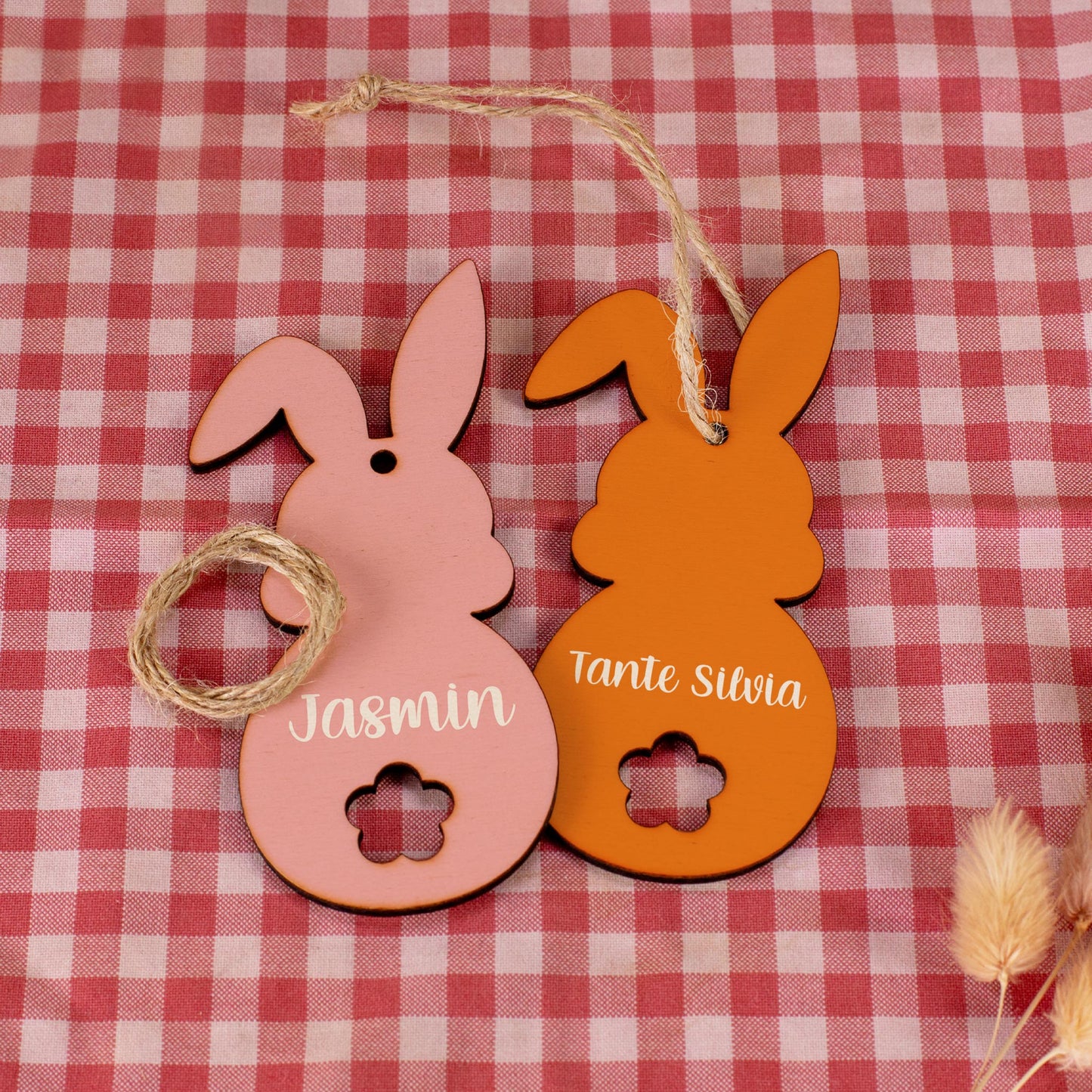 Zwei Holzanhänger in Hasenform in Rosa und Orange, bedruckt mit Namen
