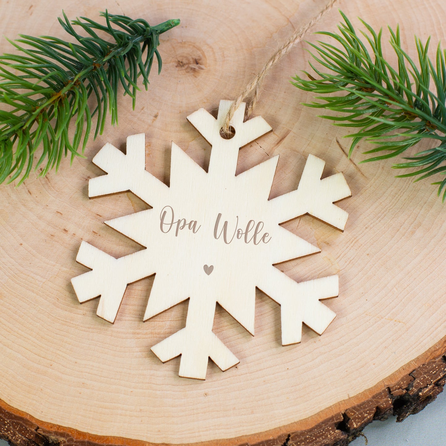 Holzanhänger Schneeflocke mit Gravur „Opa Wolle“ und Herzsymbol, liegend auf Holzscheibe mit Zweigen.