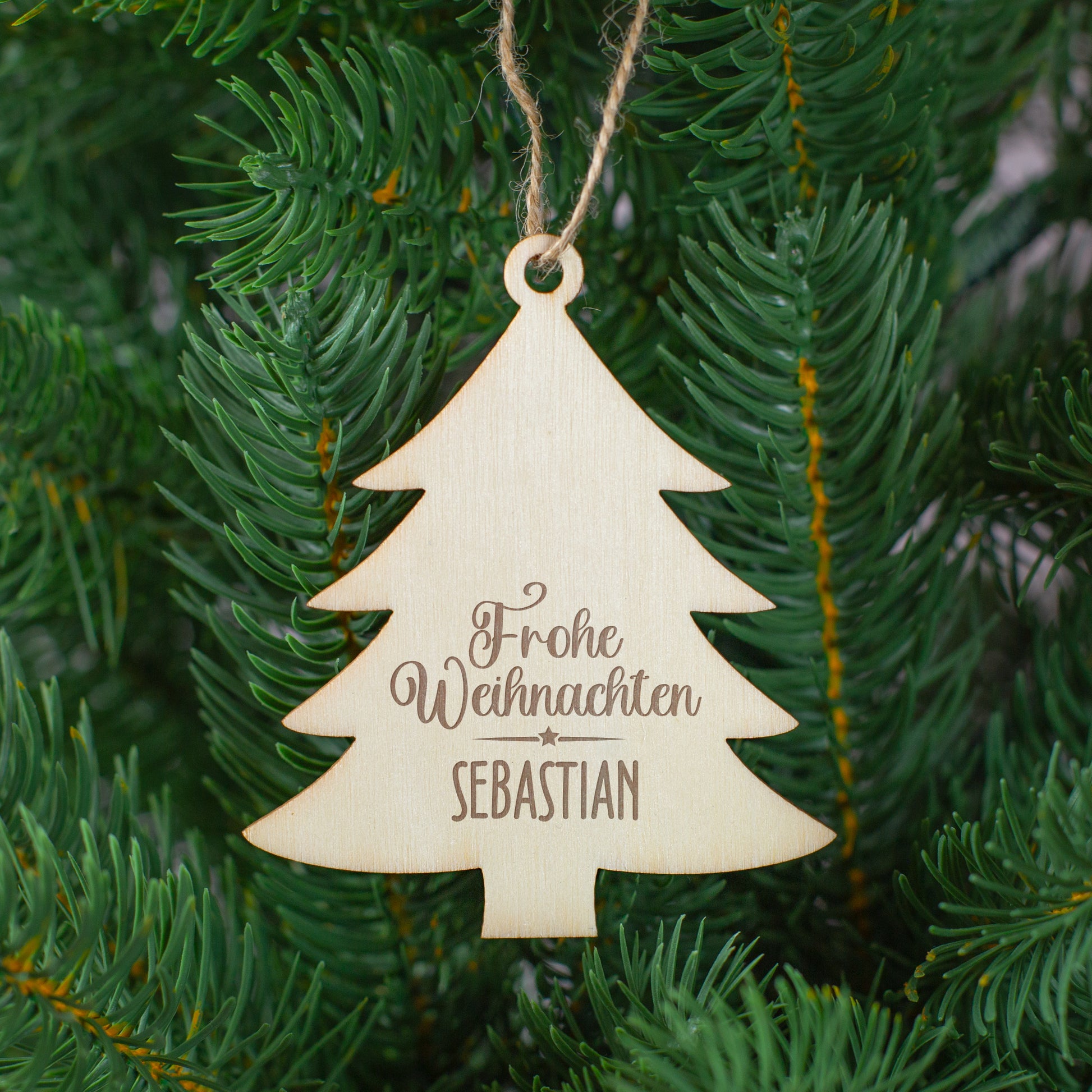 Tannenbaum-Anhänger aus Holz mit Gravur „Frohe Weihnachten Sebastian“, aufgehängt im grünen Christbaum.