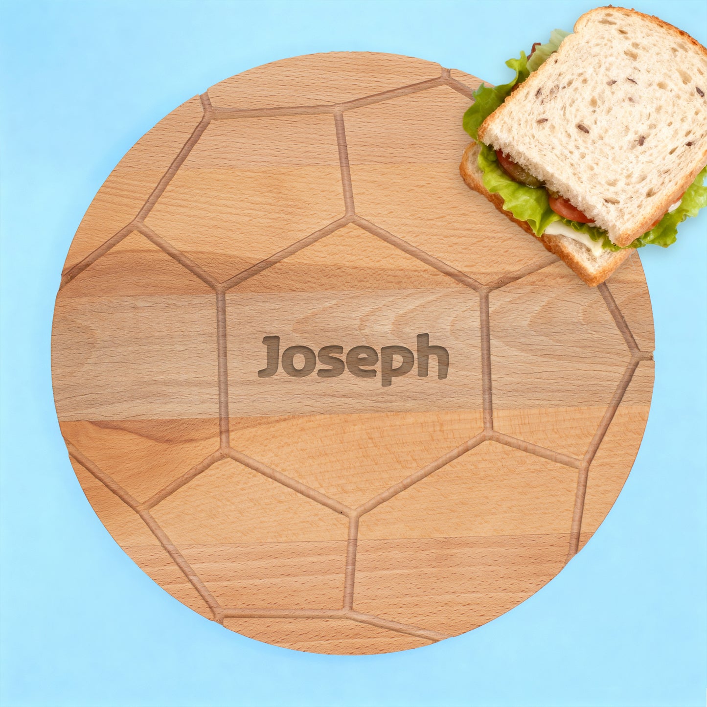 Rundes Buchenholzbrett mit Fußballmuster und graviertem Namen Joseph auf blauem Hintergrund