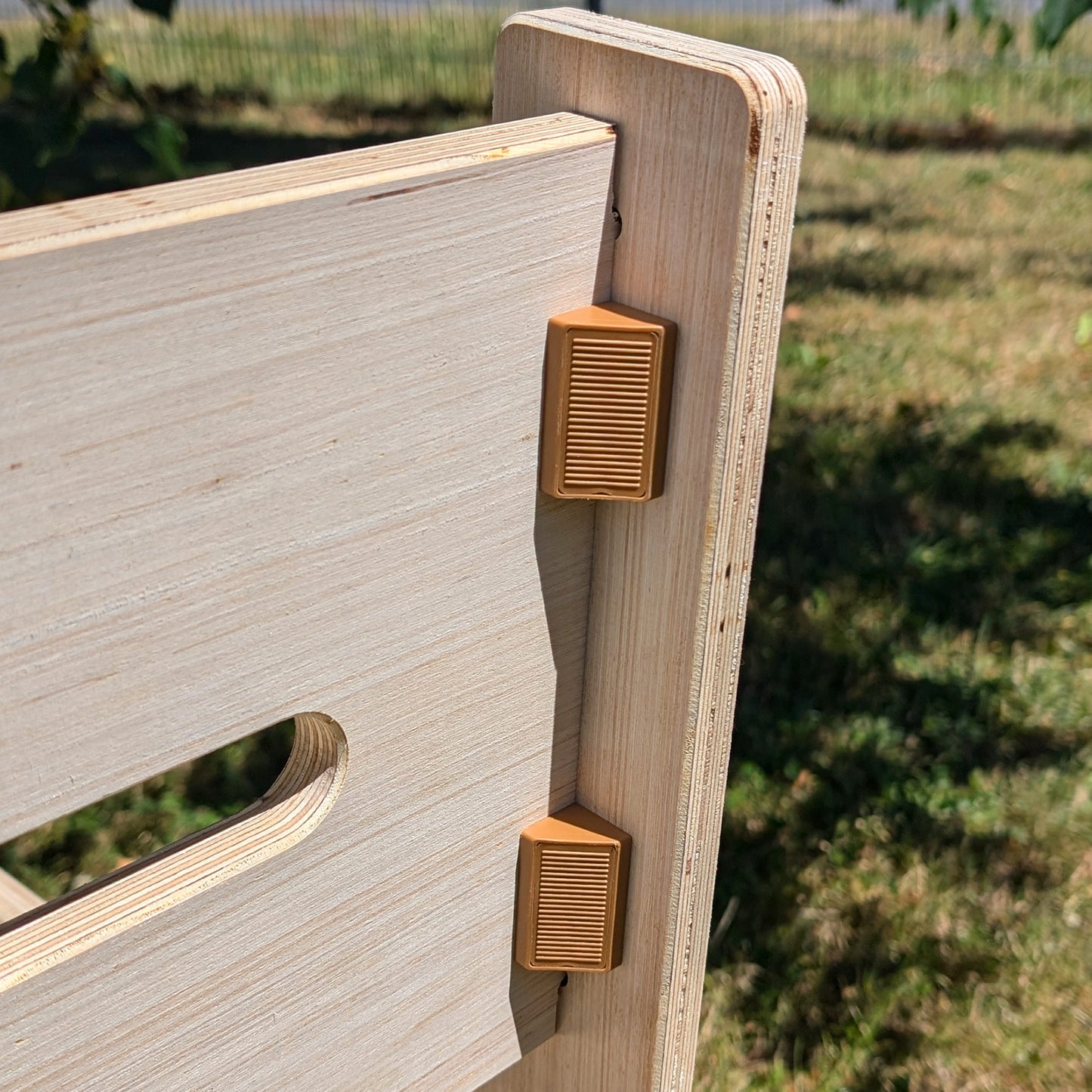 Detailansicht zweier brauner Kunststoff-Clipverbinder an der Rückenlehne der Holzbank, draußen bei Sonnenschein