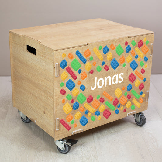 Personalisierte Rollbox aus Holz mit buntem Bausteinwelt-Motiv und Name, geschlossene Spielzeugkiste auf Rollen im Kinderzimmer
