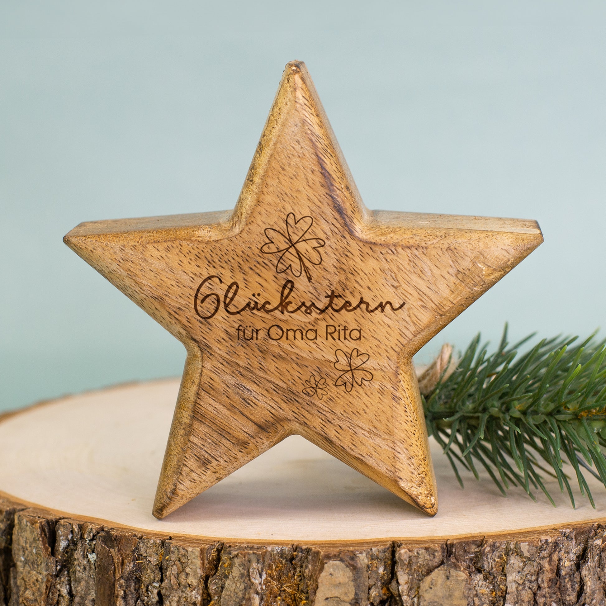 Dekorativer Glücksstern aus Holz mit Gravur auf Baumscheibe neben Tannenzweig