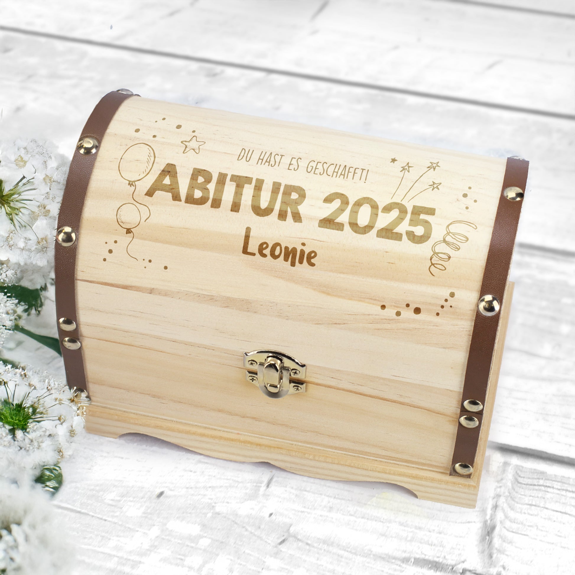 Kleine Truhe mit Gravur „Abitur 2025 Leonie“ auf weißem Holzuntergrund und Blumen