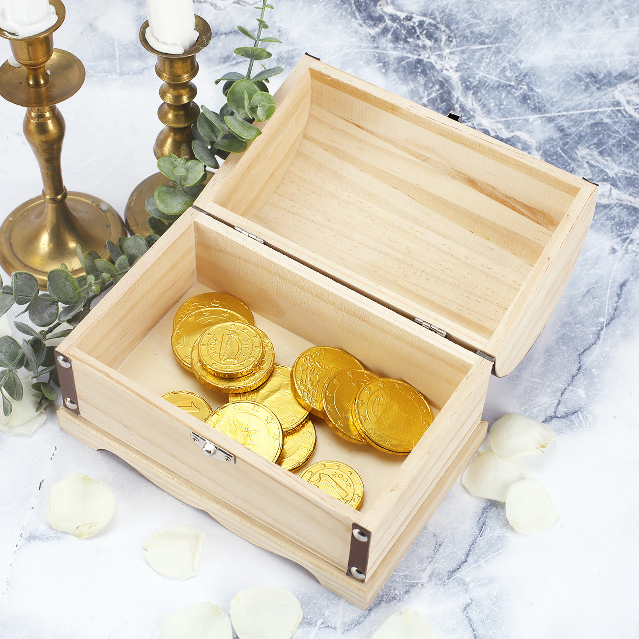 Geöffnete Truhe mit goldenen Schokomünzen, dekoriert mit Eukalyptus und Kerzenständern