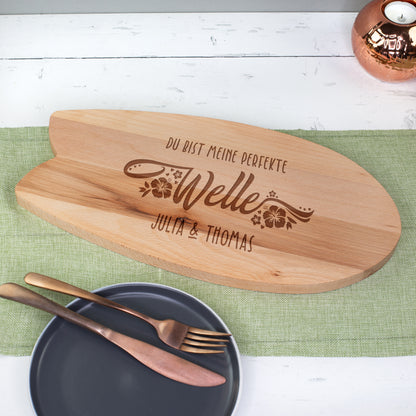 Holz-Servierbrett in Surfbrettform mit Gravur „Du bist meine perfekte Welle“ und Namen – Nahaufnahme auf Tisch mit Teller und Besteck