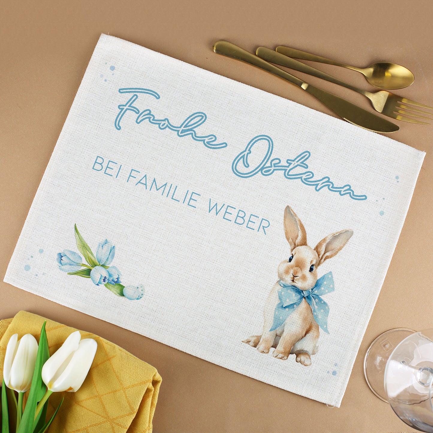 Personalisiertes Platzdeckchen aus Jute mit Hasenmotiv, Wunschtext und Frühlingsdesign neben Besteck, Tulpen und Glas
