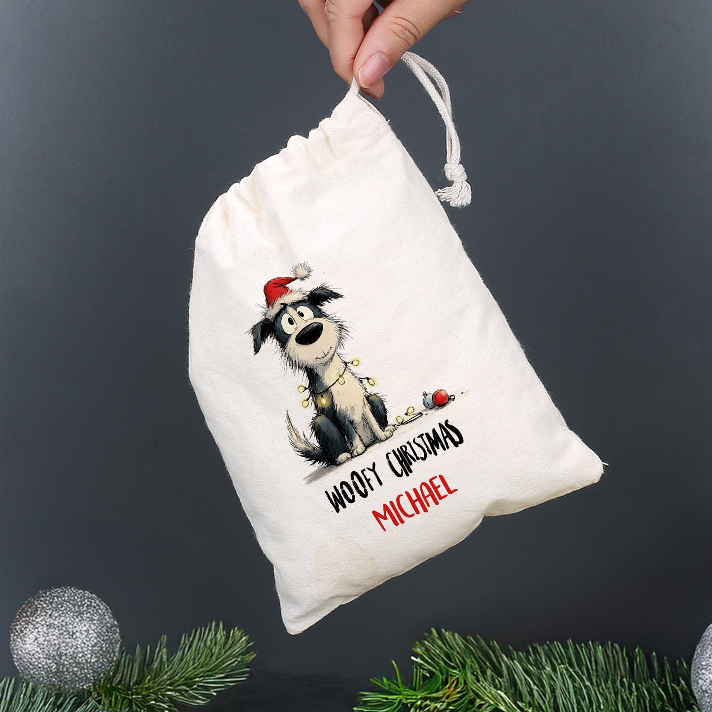 Kleiner Baumwollbeutel mit Hund in Weihnachtsmütze und Aufdruck „Woofy Christmas – Michael“, gehalten von einer Hand