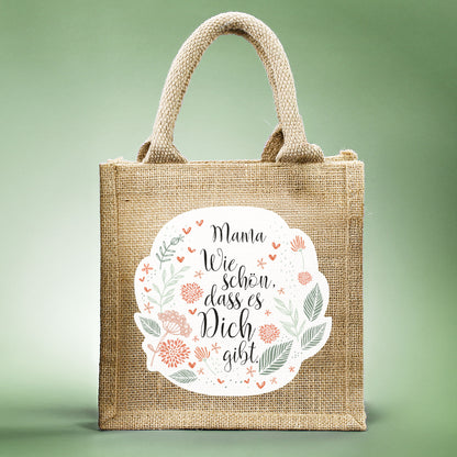 Geschenktasche aus Jute mit floralem Design, dem Spruch „Wie schön, dass es dich gibt.“ und personalisiertem Namen, frontal fotografiert.