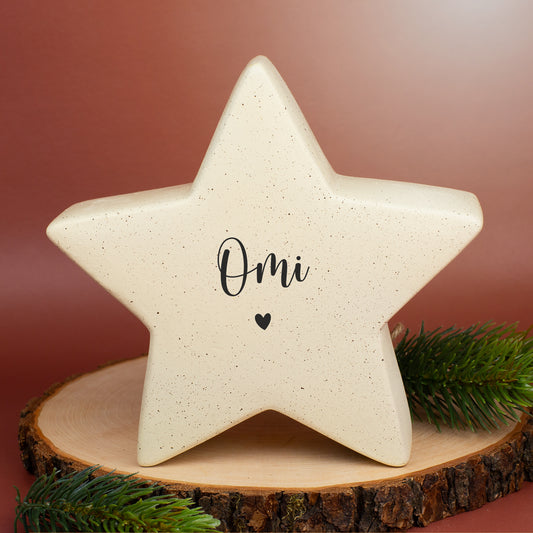 Großer Keramikstern in Creme mit dem Aufdruck „Omi“ und Herzmotiv, auf Holzplatte und Tannenzweig dekoriert.
