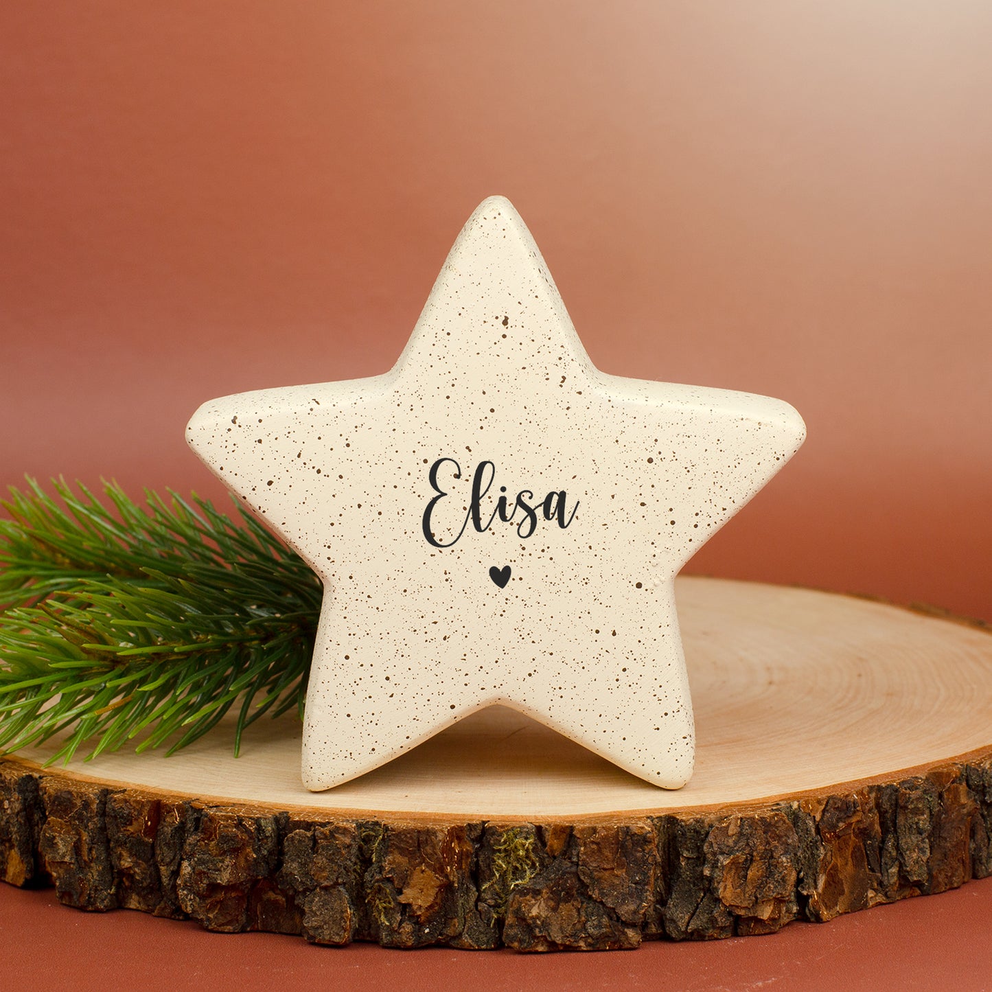 Kleiner Keramikstern in Creme mit Personalisierung „Elisa“ und Herzmotiv, dekoriert mit Tannenzweig.