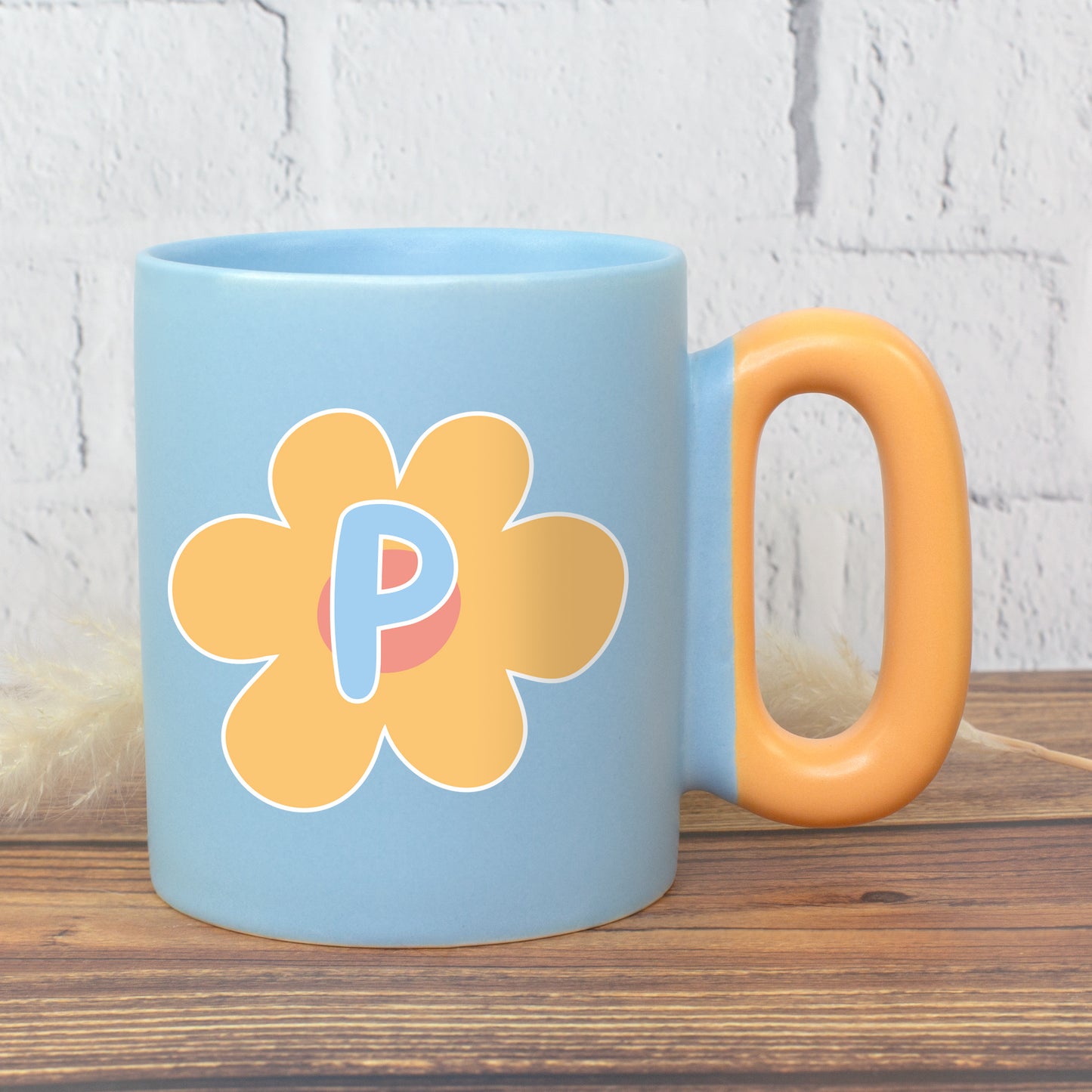 Blaue Tasse mit gelber Blume und Initiale P sowie ovalem Griff auf Holzuntergrund