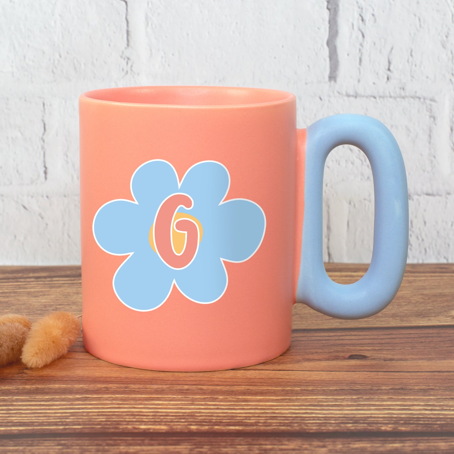 Korallfarbene Tasse mit blauer Blume und Initiale G auf Holzfläche
