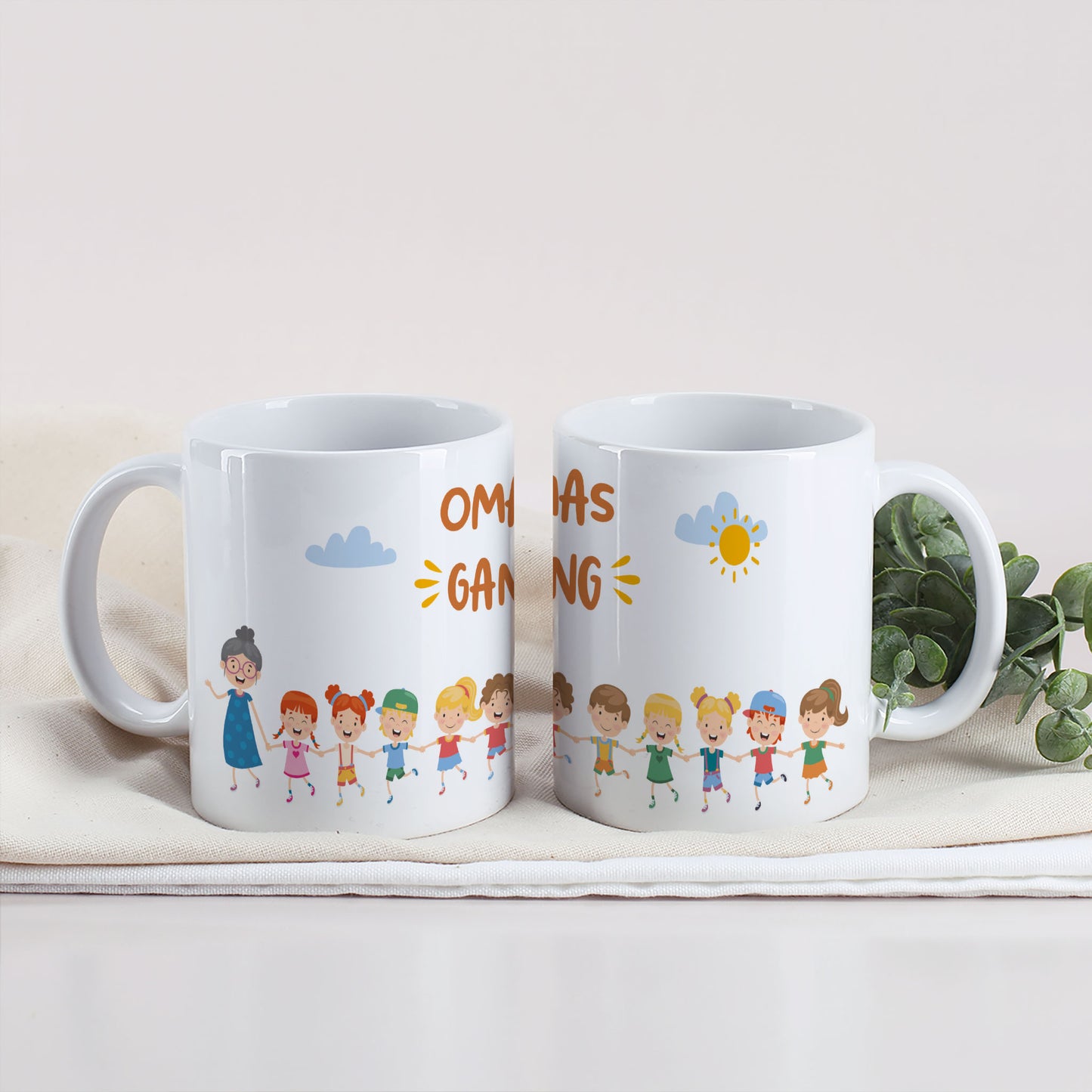Zwei Tasse mit Motiv „Omas Gang“, Oma und eine Gruppe Kinderfiguren, auf einem weißen Tuch mit Eukalyptuszweig.