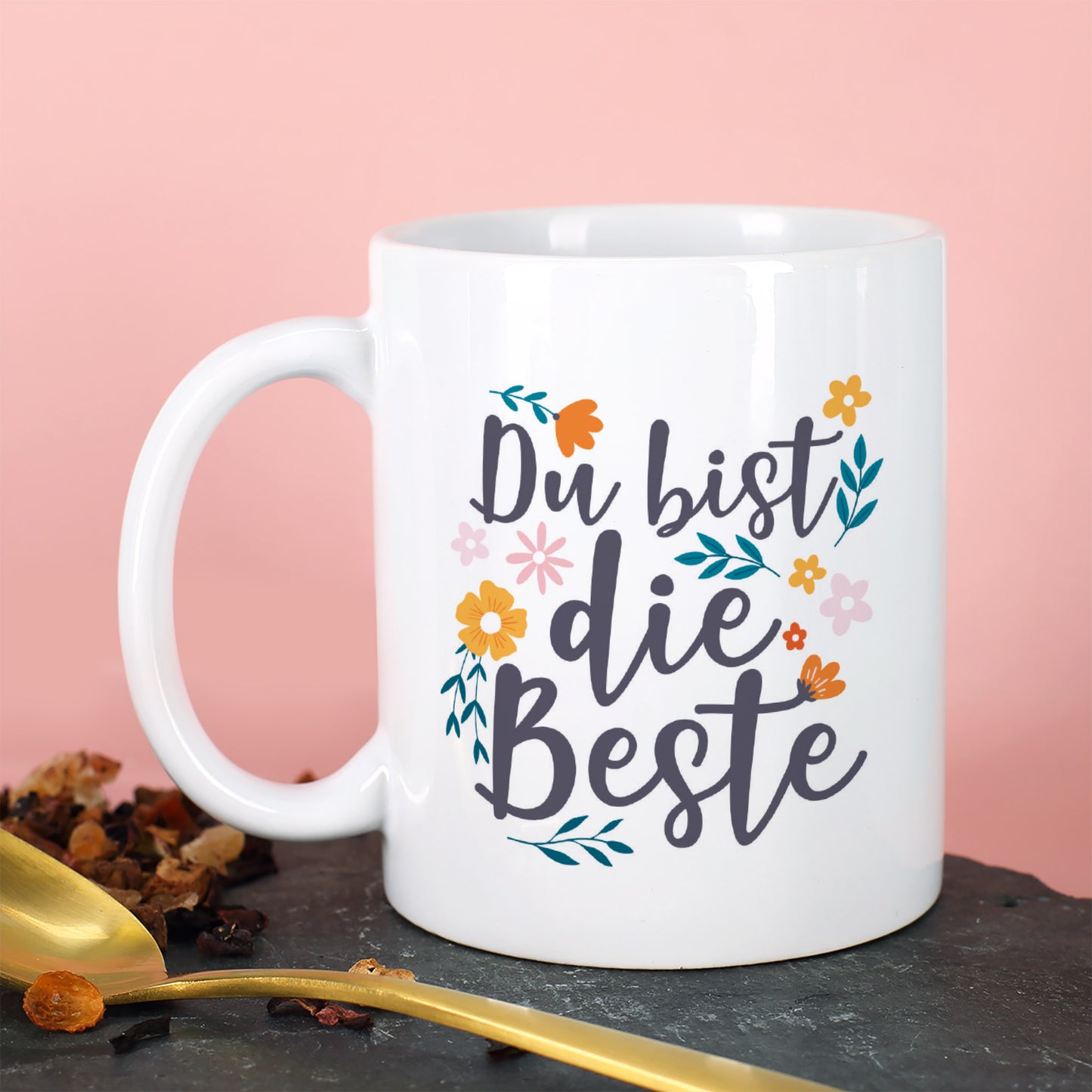 Detailaufnahme der Tasse mit dem Spruch „Du bist die Beste“ auf rosa Hintergrund mit Löffel