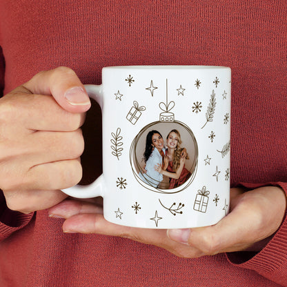 Weiße Fototasse mit Weihnachtskugel-Design in Schwarz und integriertem Foto – festlich mit Sternen und Geschenken dekoriert.