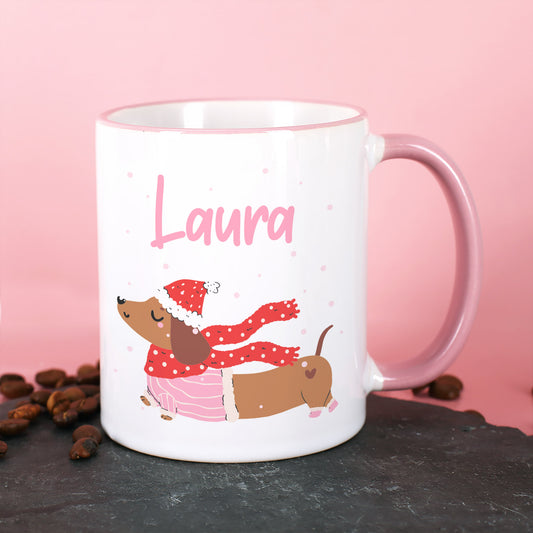 Weiße Tasse mit Dackel im Winteroutfit und personalisiertem Namen, rosa Hintergrund